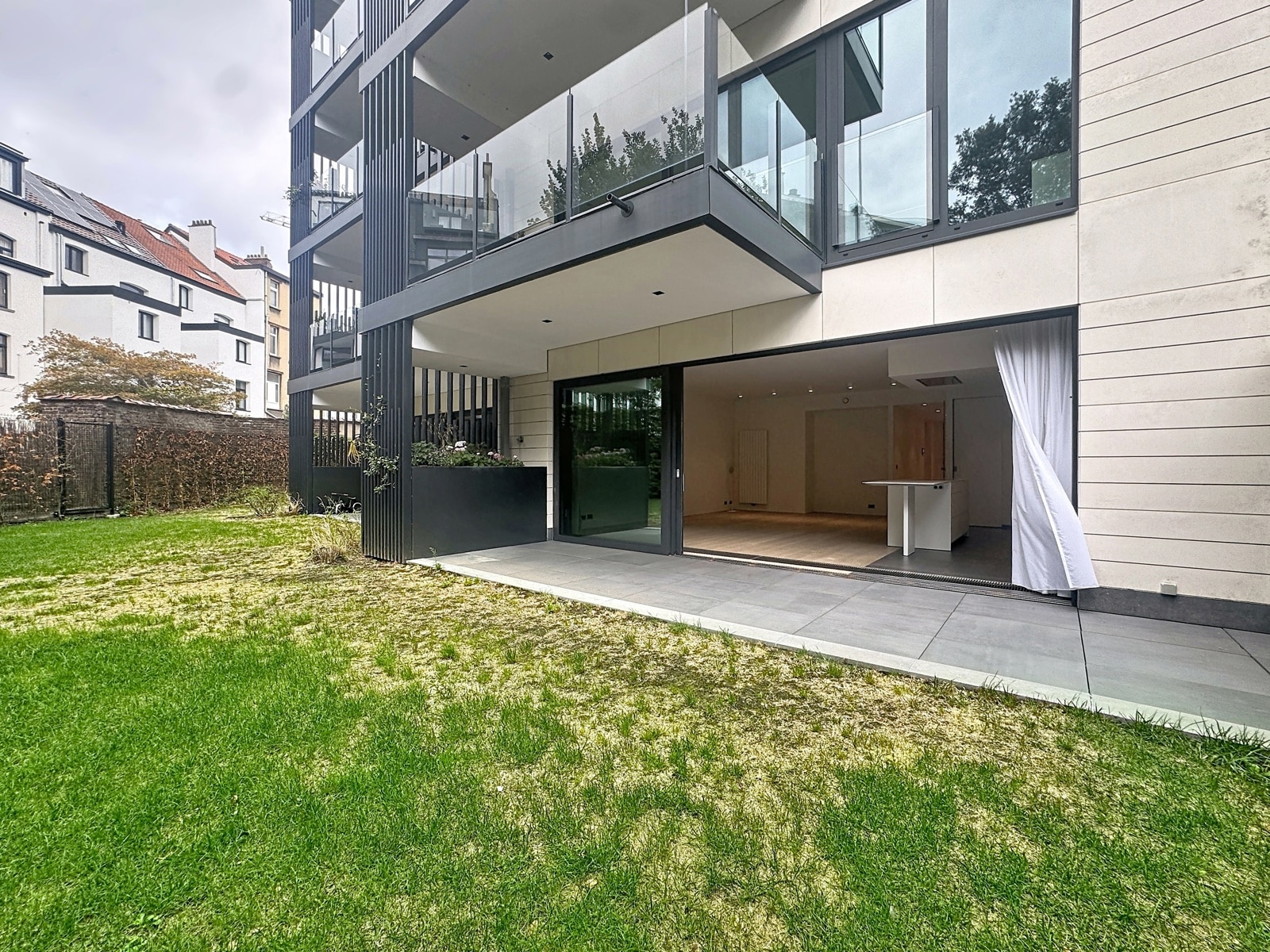 Façade Moderne avec Jardin Privatif – You Real Estate Agency Appartement moderne avec terrasse, jardin privatif et salon ouvert avec cuisine équipée.