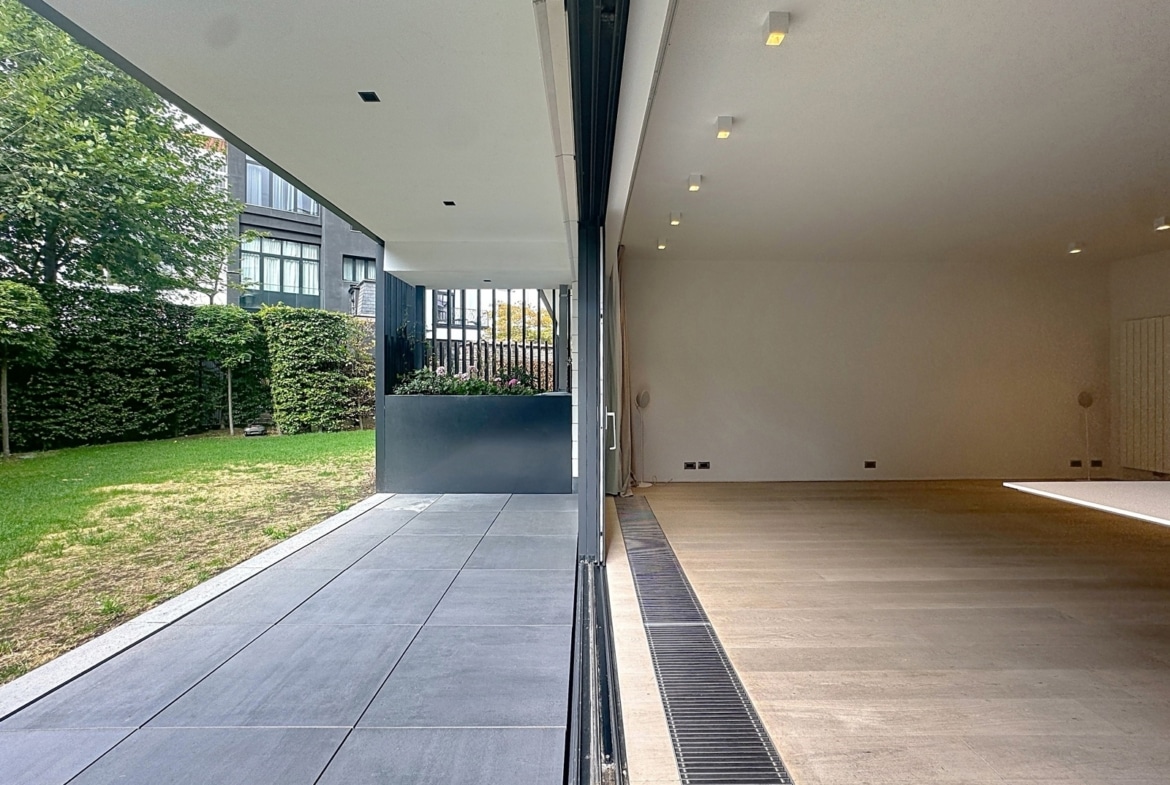 Salon moderne ouvert sur terrasse et jardin verdoyant dans maison contemporaine.