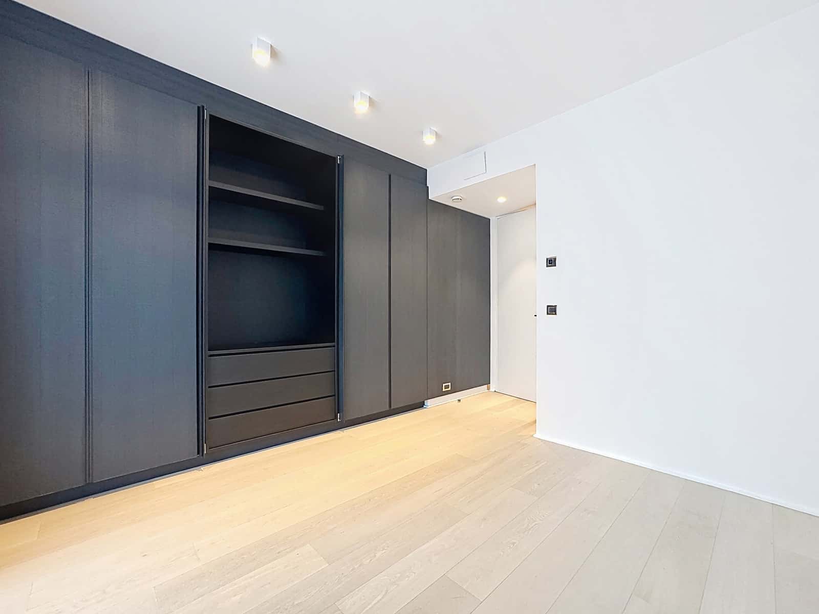 Dressing Moderne Intégré – You Real Estate Agency Dressing moderne avec placards intégrés sombres et parquet clair dans appartement.