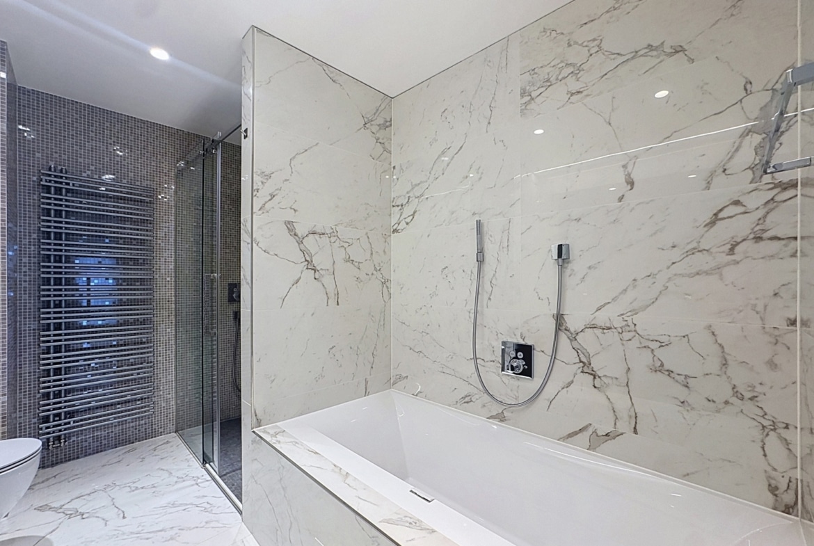 Salle de bains luxueuse en marbre avec baignoire et douche vitrée dans appartement moderne.