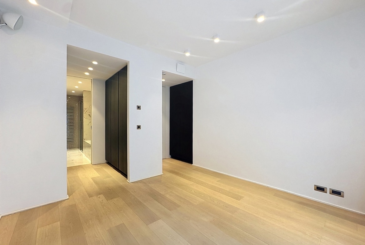 Salon moderne vide avec parquet clair, spots encastrés et rangements intégrés dans appartement.
