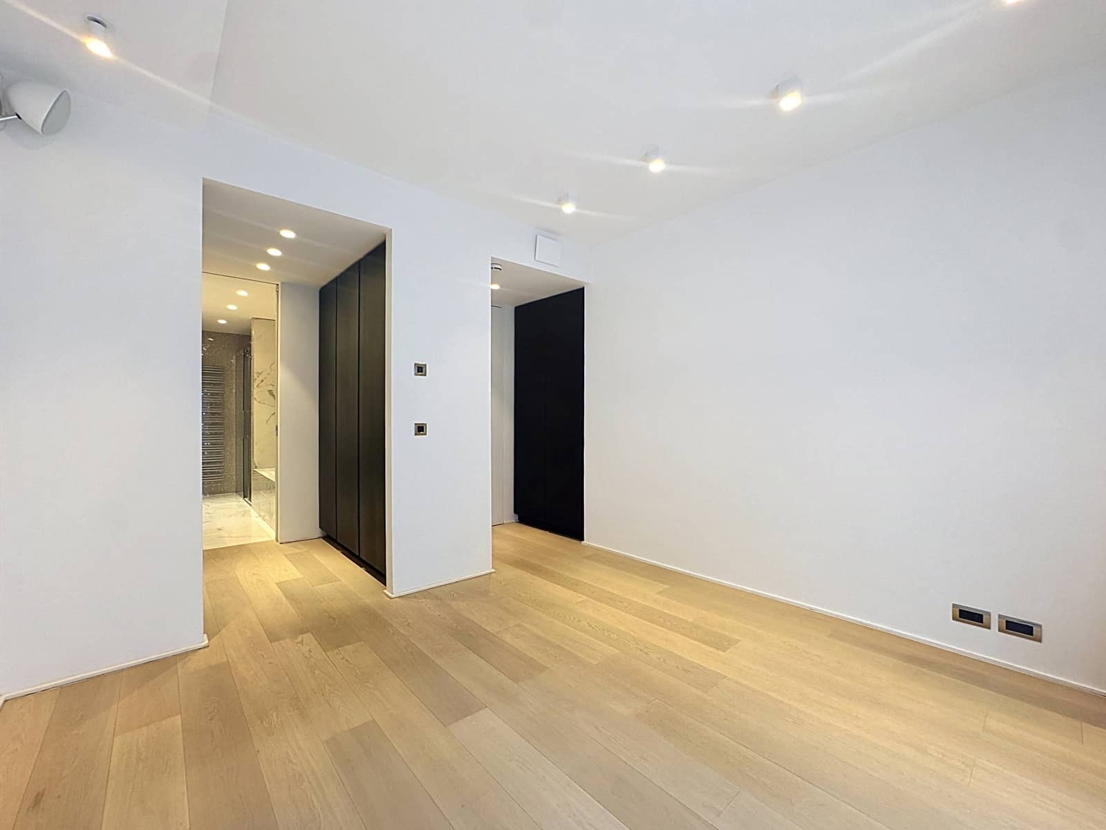 Salon Moderne Lumineux – You Real Estate Agency Salon moderne vide avec parquet clair, spots encastrés et rangements intégrés dans appartement.