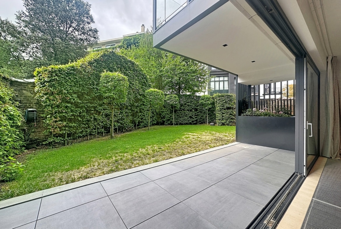 Terrasse moderne avec jardin paysager et baie vitrée d’une maison contemporaine.