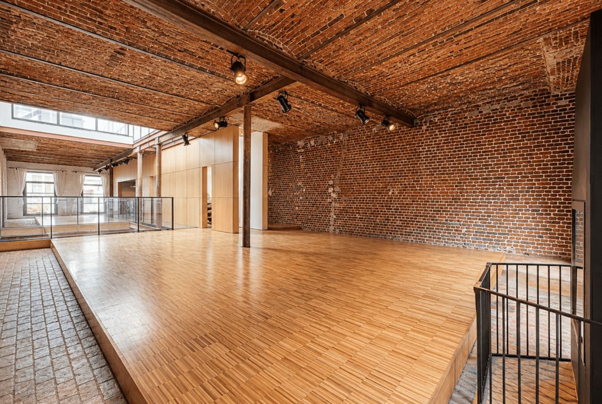 Appartement loft rénové avec murs en briques, plafond voûté et plancher bois.