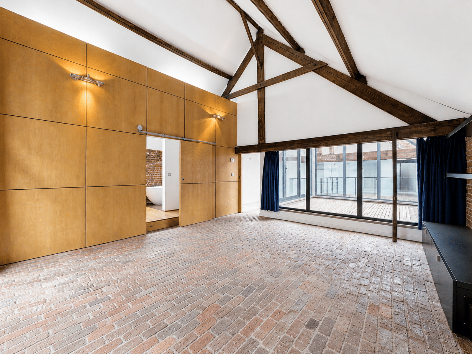 Salon Loft avec Poutres Apparentes – You Real Estate Agency Grand salon loft avec plafond voûté, poutres apparentes, briques et terrasse vitrée.