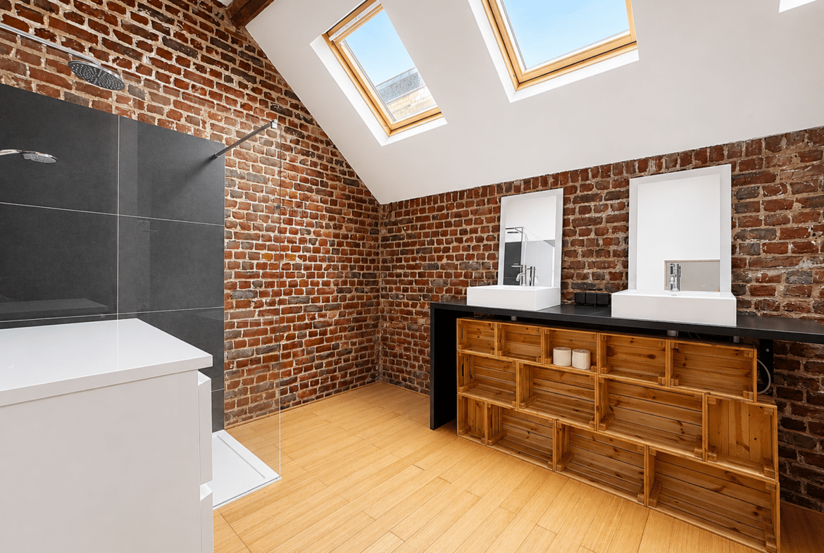 Salle de bain moderne sous combles avec briques apparentes et puits de lumière.