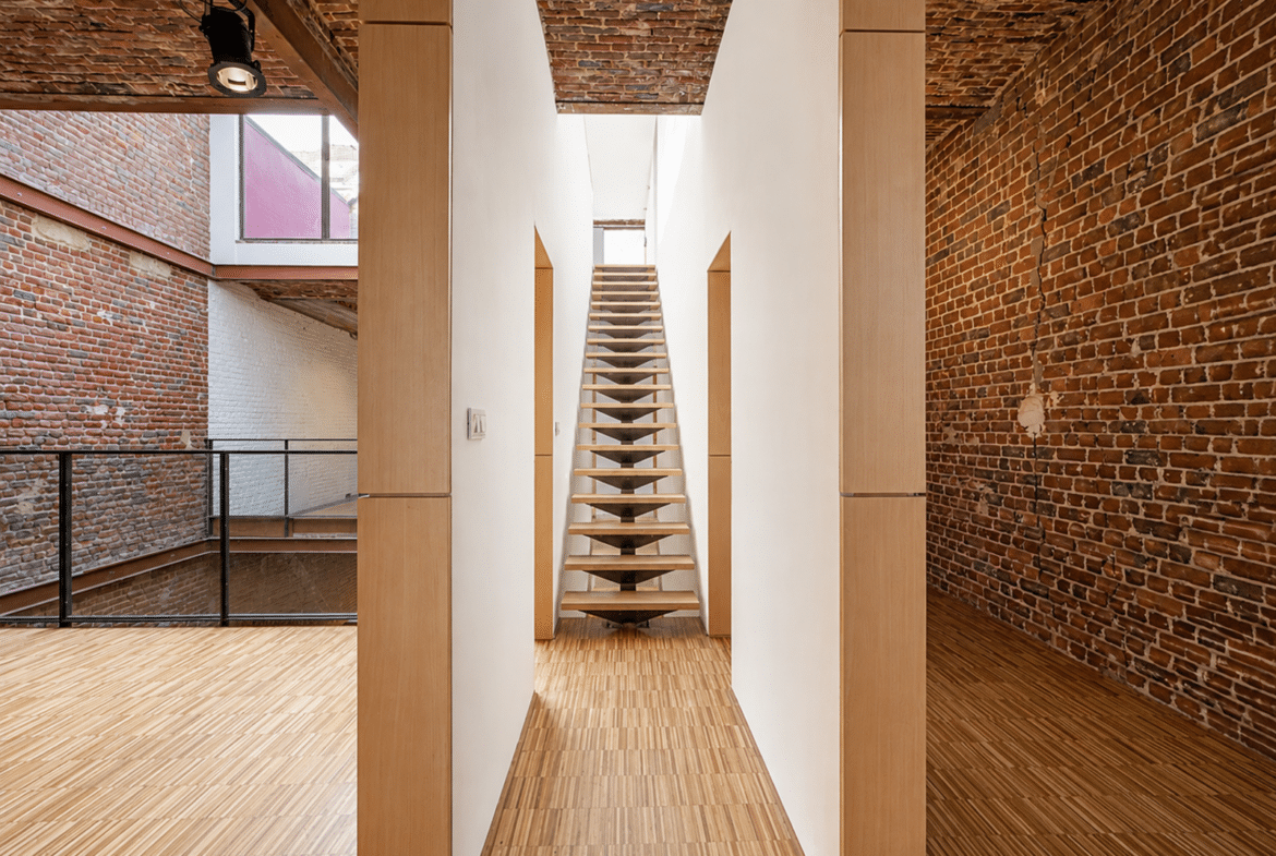Appartement loft avec escalier flottant, murs en briques apparentes et parquet bois.