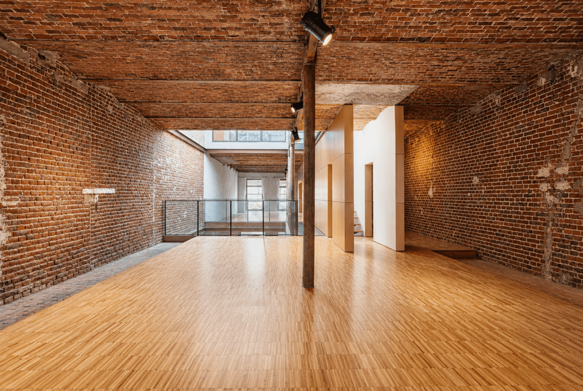 Loft rénové avec murs en briques apparentes, parquet clair et mezzanine vitrée.