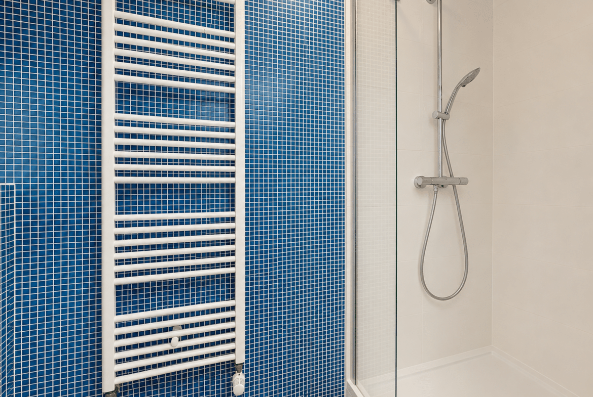 Salle de bain moderne d’appartement avec douche vitrée et carrelage bleu.