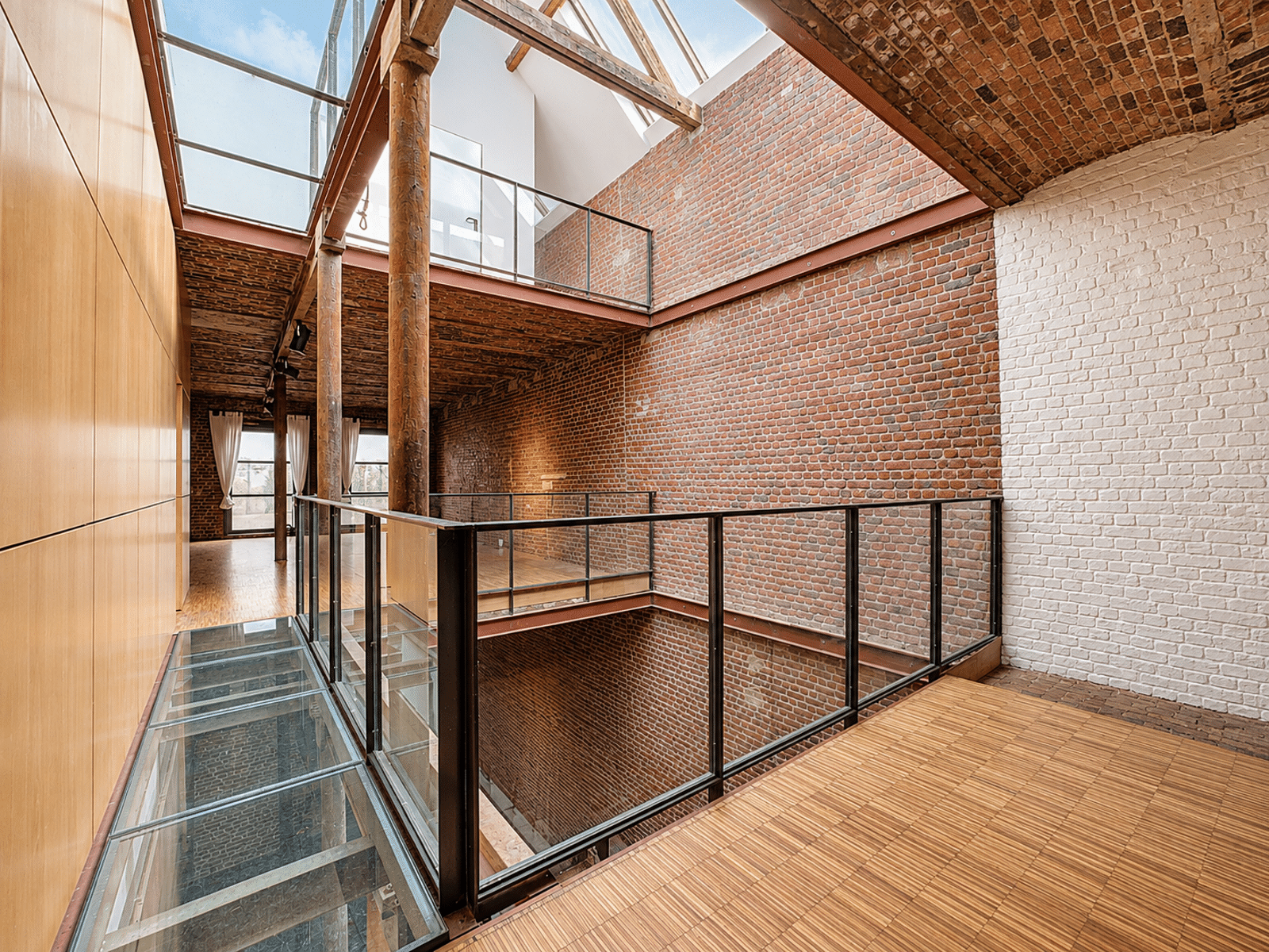 Atrium Lumineux de Loft Rénové – You Real Estate Agency Atrium lumineux d’un loft rénové avec murs en briques, verrière et passerelles vitrées.