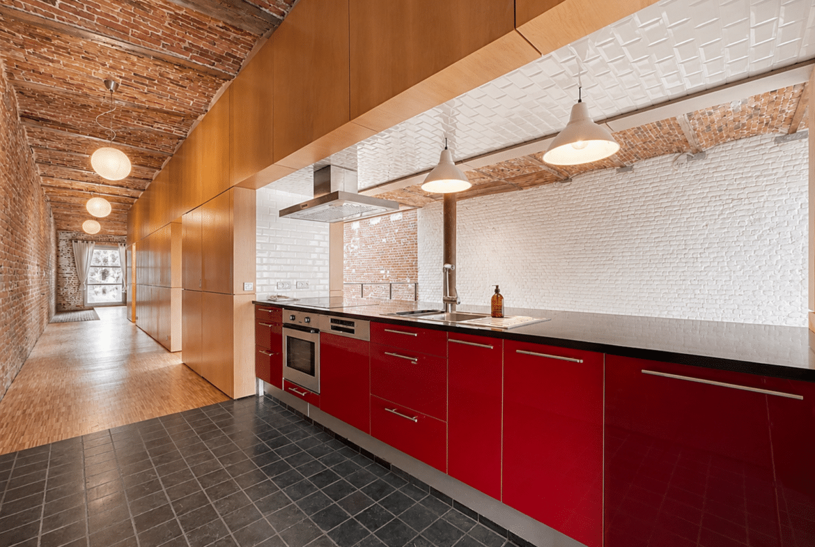 Cuisine moderne rouge dans appartement loft avec briques apparentes et poutres.