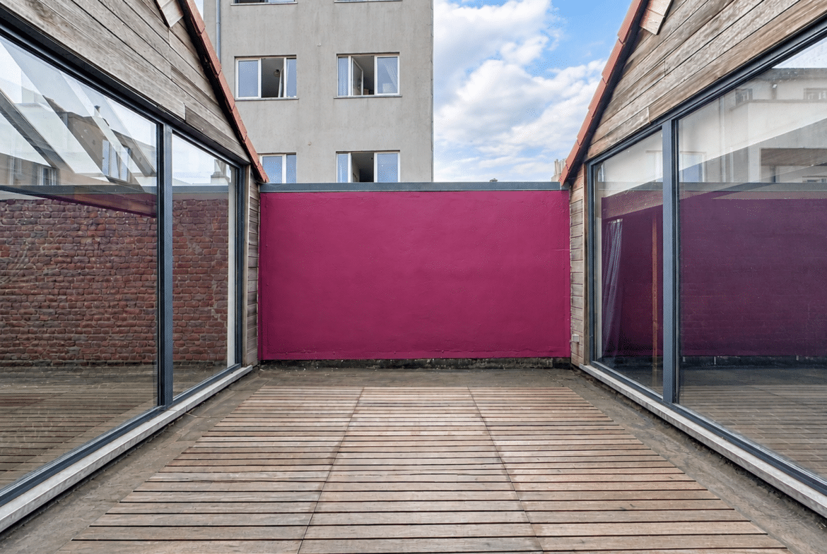 Terrasse intérieure moderne avec bardage bois, baies vitrées et mur rose.