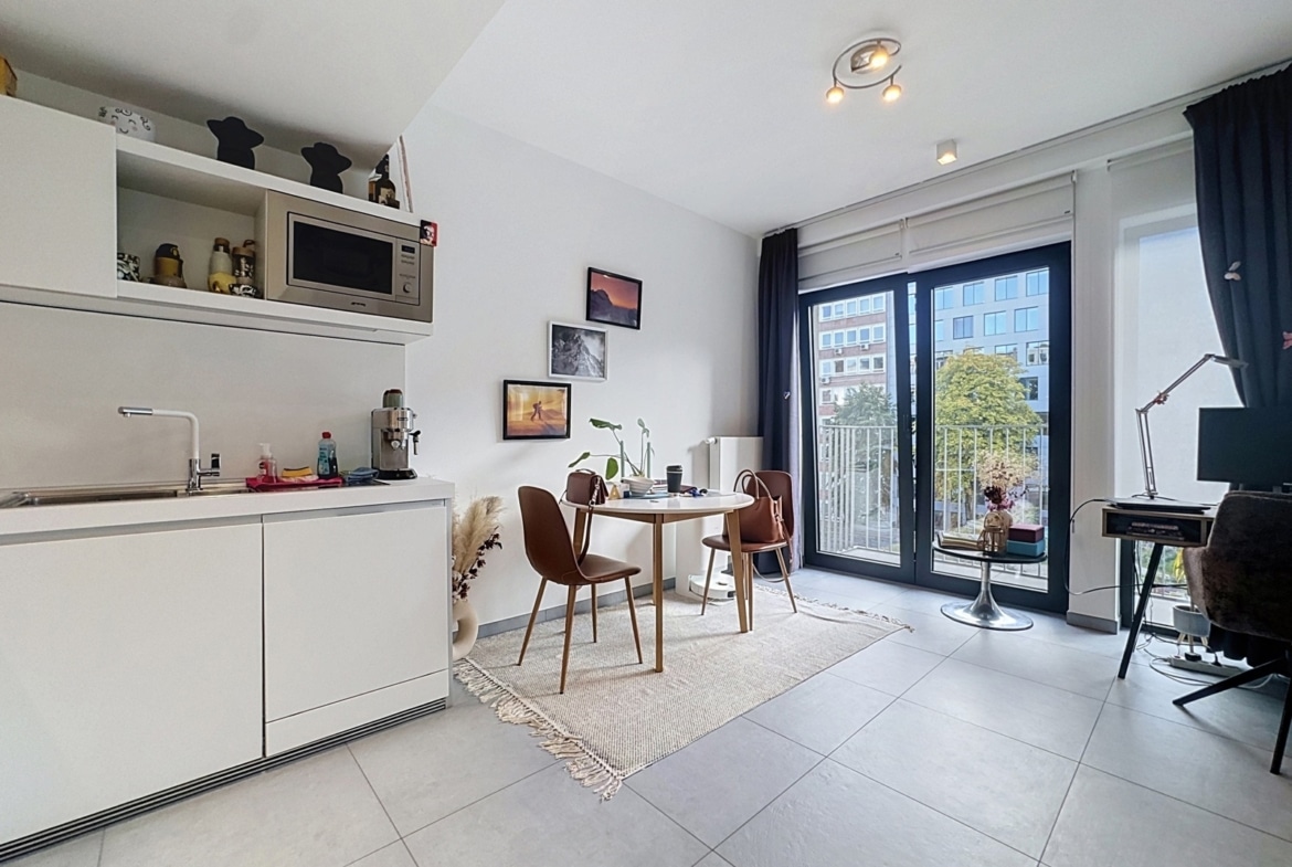 A bright, open-concept kitchen and dining area with white cabinets, a microwave, and a small round table set for two near a balcony door.