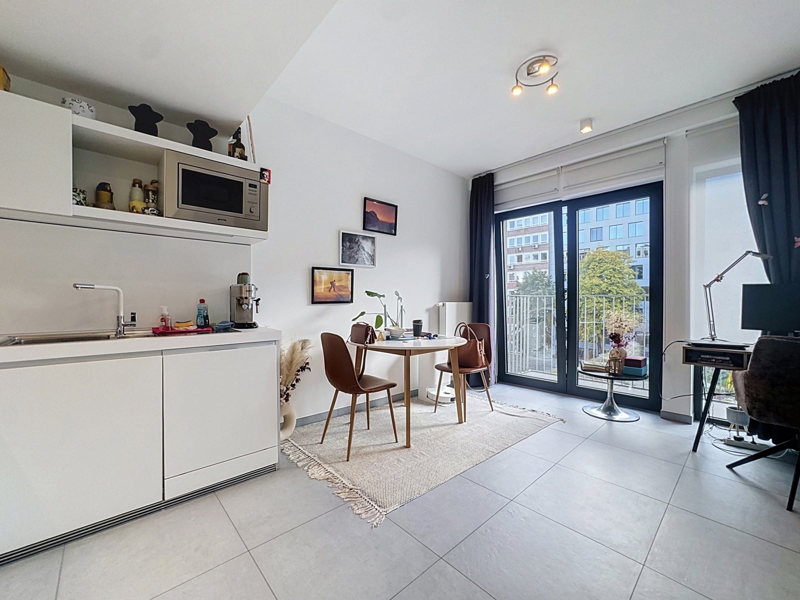 whise photo 4 A bright, open-concept kitchen and dining area with white cabinets, a microwave, and a small round table set for two near a balcony door.