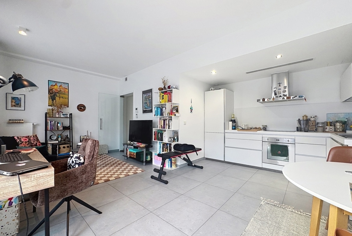 Bright, open-concept living area and white kitchen with a sofa, bookshelf, and exercise bench.