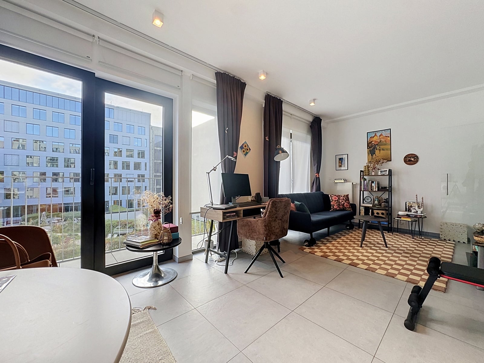 whise photo 7 A bright living room with large glass doors leading to a balcony, a home office set up by the window, and a cozy seating area.