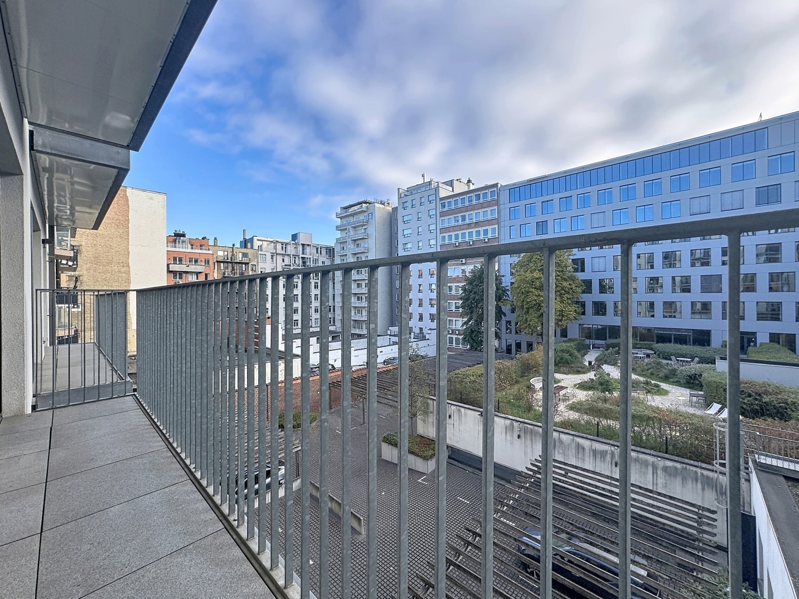 Modern Balcony with a View of the Courtyard – You Real Estate Agency Modern apartment terrace with a view of an inner courtyard and city buildings.