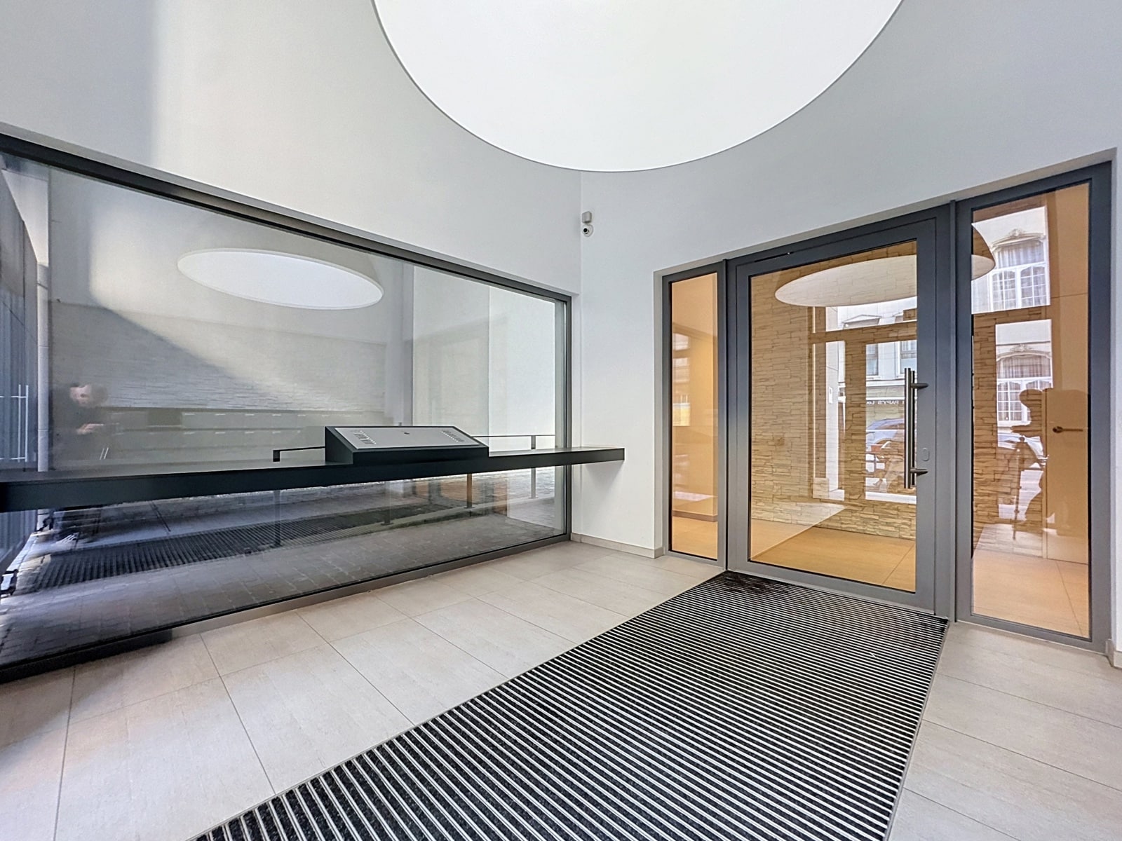 Modern, Glass-Enclosed Entryway – You Real Estate Agency Modern building lobby with glass doors and light-colored tile flooring.