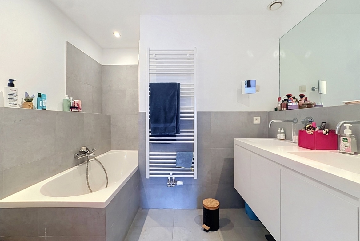 Modern apartment bathroom with a bathtub, wall-mounted sink, and large mirror.