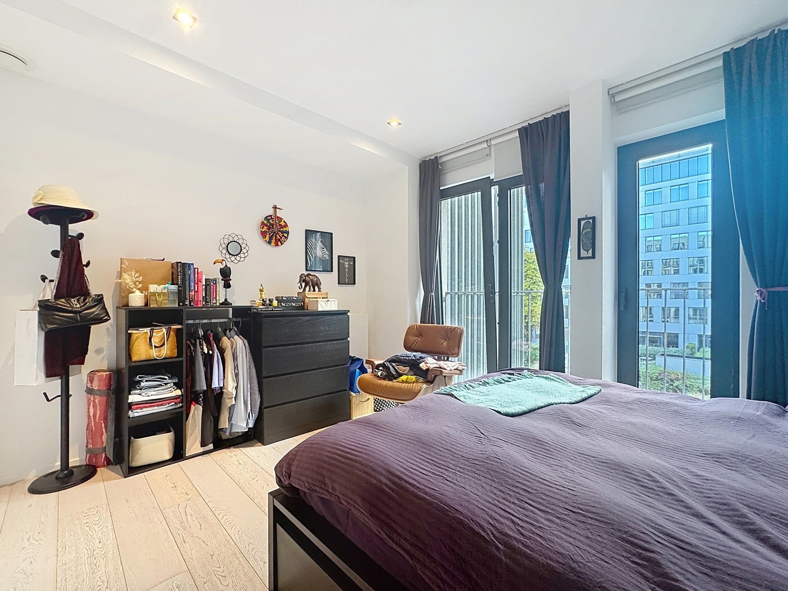 Bright Room with Floor-to-Ceiling Windows – You Real Estate Agency A bright bedroom in a modern apartment with a double bed, storage space, and large picture windows.