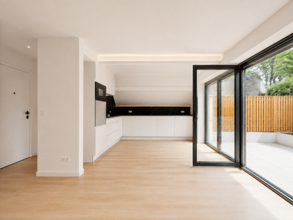 Lichte, moderne keuken met witte kasten, een achterwand van zwart marmer en een grote glazen schuifdeur die uitkomt op een met houten hekken omheind terras   appartement met 2 slaapkamers  Waterloo