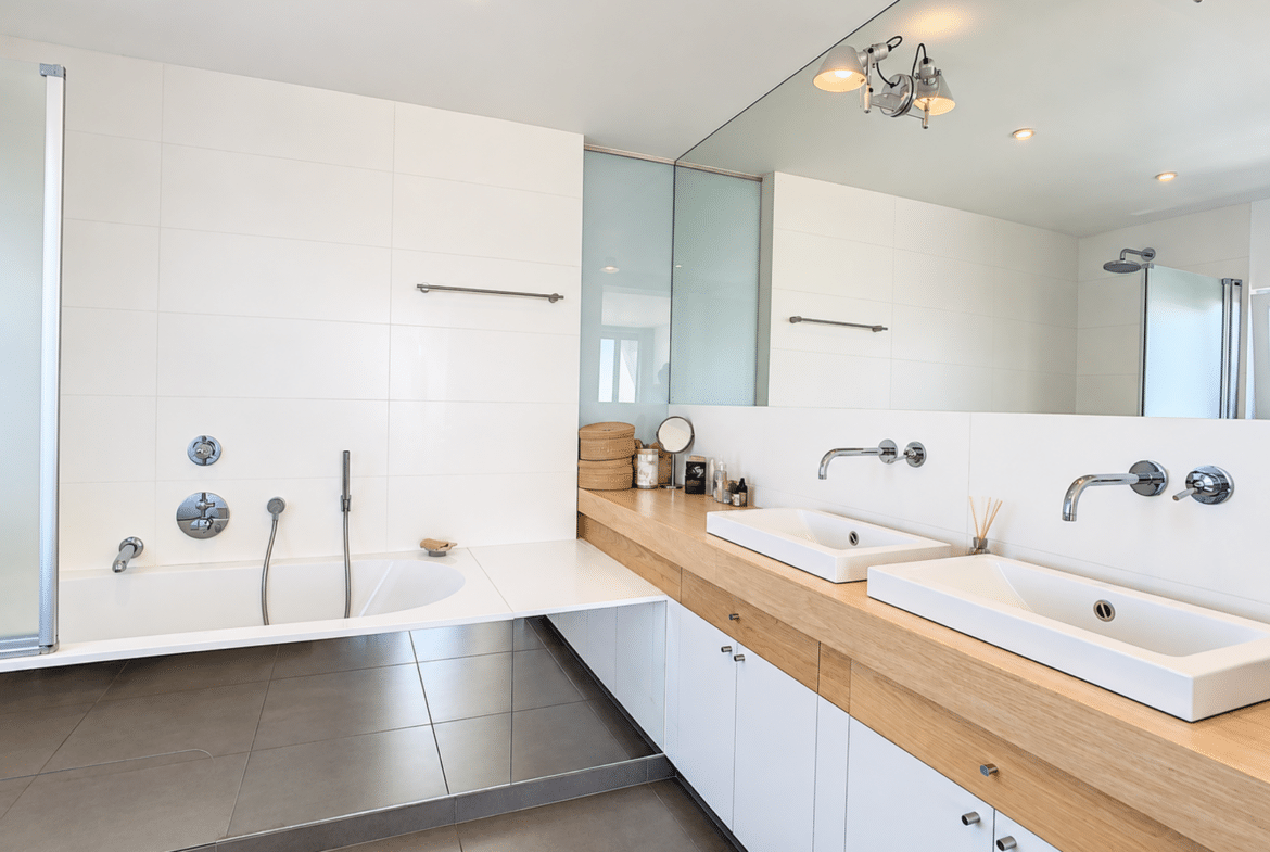 Modern bathroom with a bathtub, double sinks, and a glass-enclosed shower in an apartment.