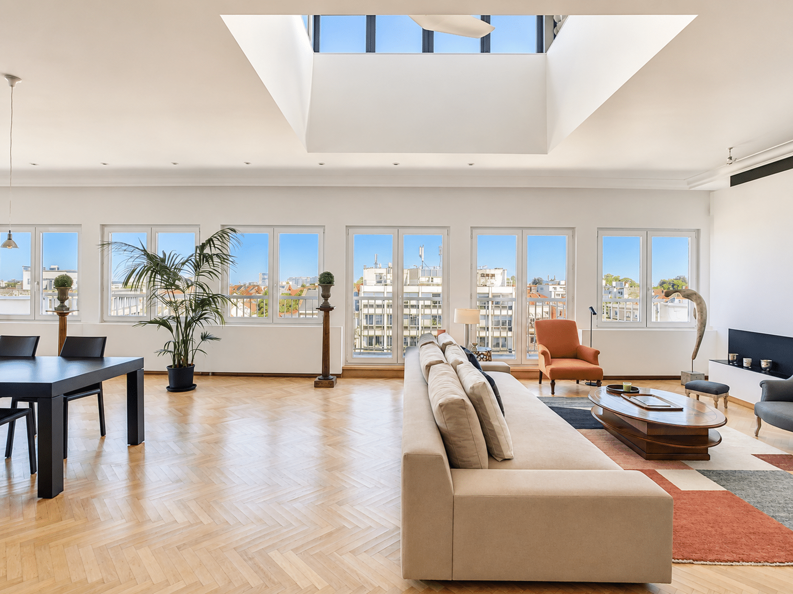 whise photo 3 A bright, open living room with a beige sectional, an orange armchair, and a wooden coffee table; large windows look out onto the city skyline.