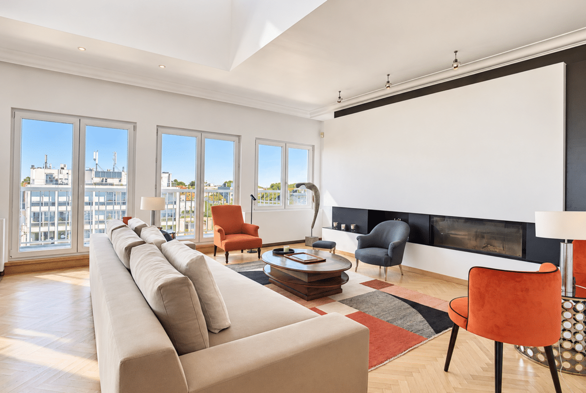 Bright living room in a modern apartment with a fireplace, large picture windows, and hardwood floors.