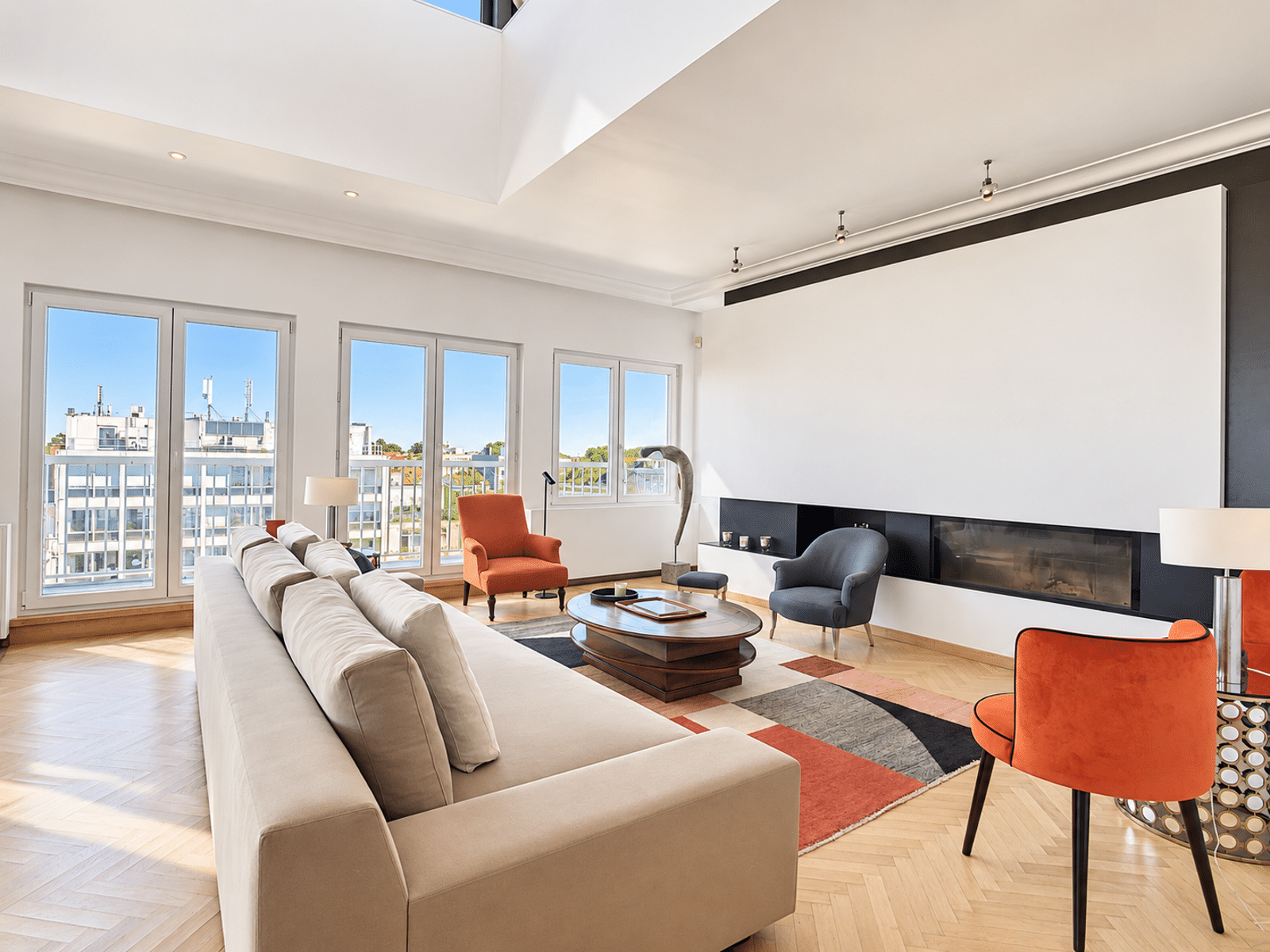 Bright living room with fireplace - You Real Estate Agency Bright living room in a modern apartment with a fireplace, large picture windows, and hardwood floors.