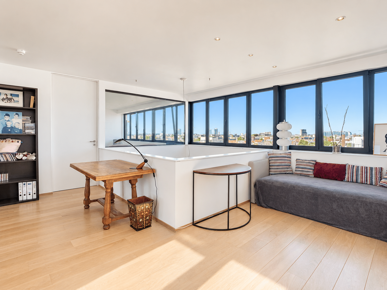Bright Living Room With Large Windows - You Real Estate Agency A bright living room in a modern apartment with large windows, light-colored hardwood floors, and a city view.
