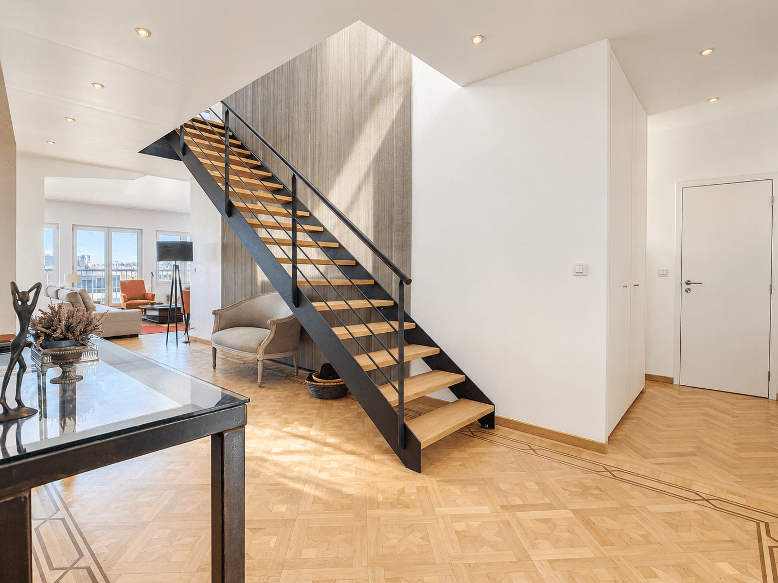 Bright Entryway with a Stylish Staircase – You Real Estate Agency Contemporary home with a stylish staircase, geometric hardwood floors, and a bright living room.