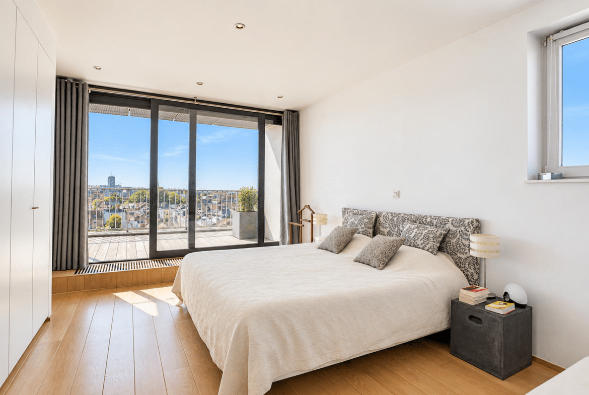 Modern apartment bedroom with a terrace, light-colored hardwood floors, and an unobstructed city view.