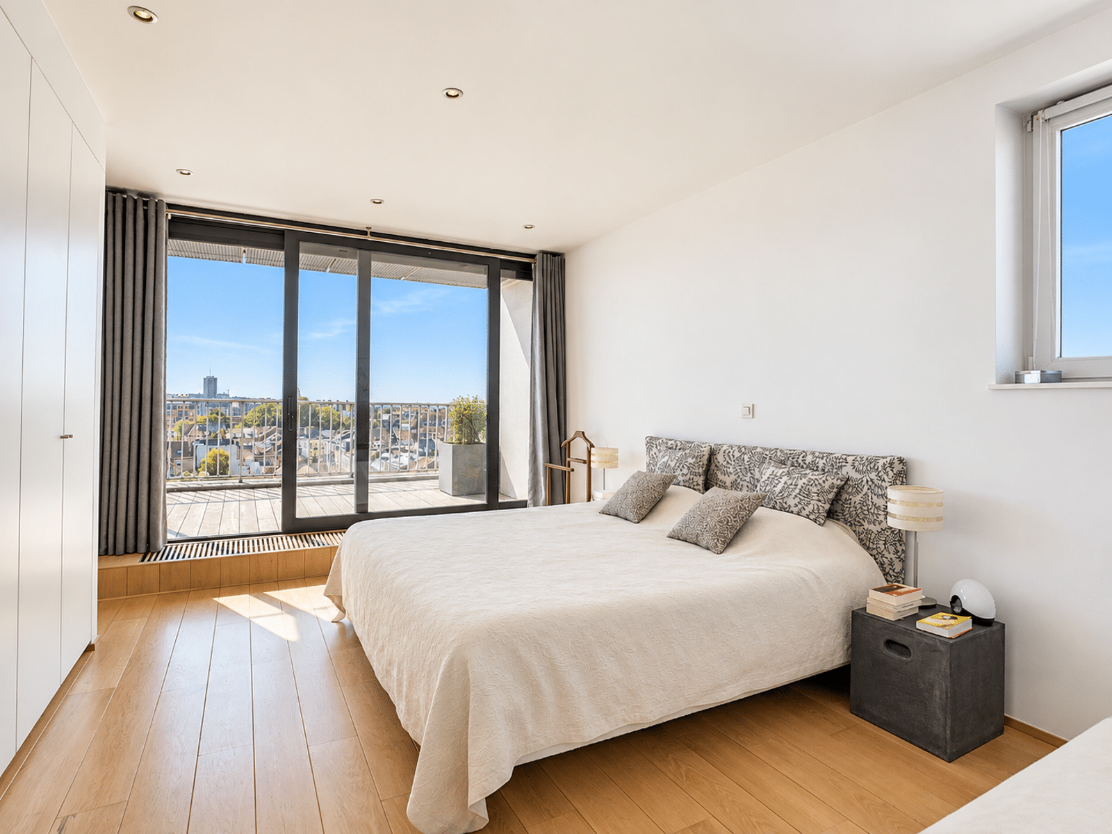Modern Room with Terrace – You Real Estate Agency Modern apartment bedroom with a terrace, light-colored hardwood floors, and an unobstructed city view.