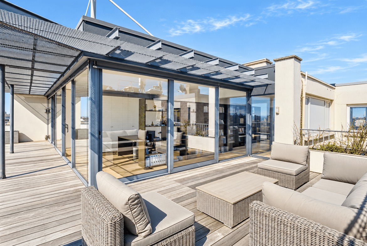 Rooftop terrace of a modern apartment with an outdoor living area and floor-to-ceiling windows.