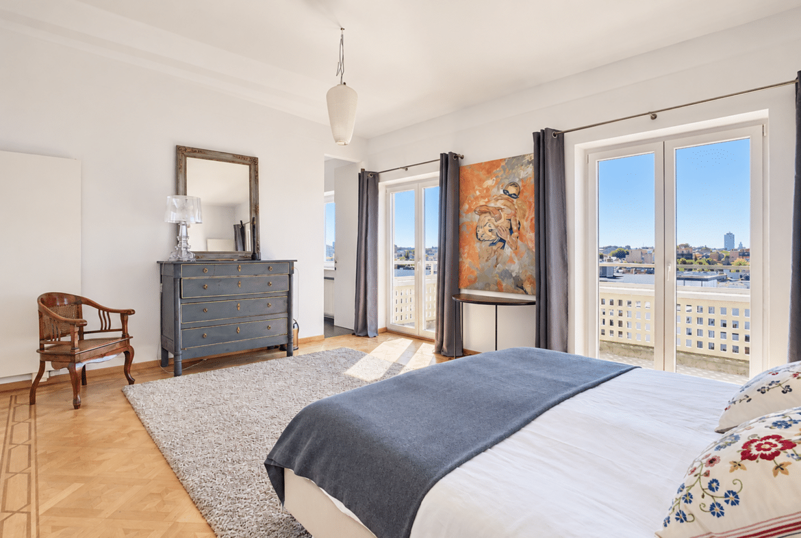 A bright apartment room with hardwood floors, a balcony, and a city view.