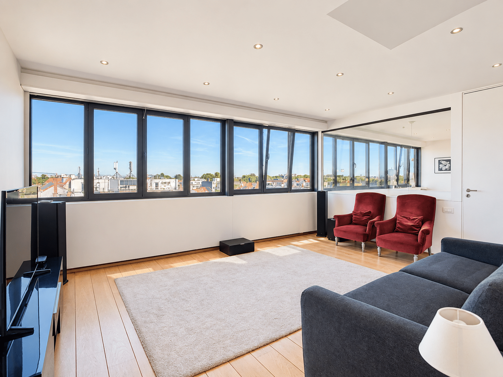 Bright Living Room with Large Windows - You Real Estate Agency A bright living room in a modern apartment with large windows, light-colored hardwood floors, and red armchairs.