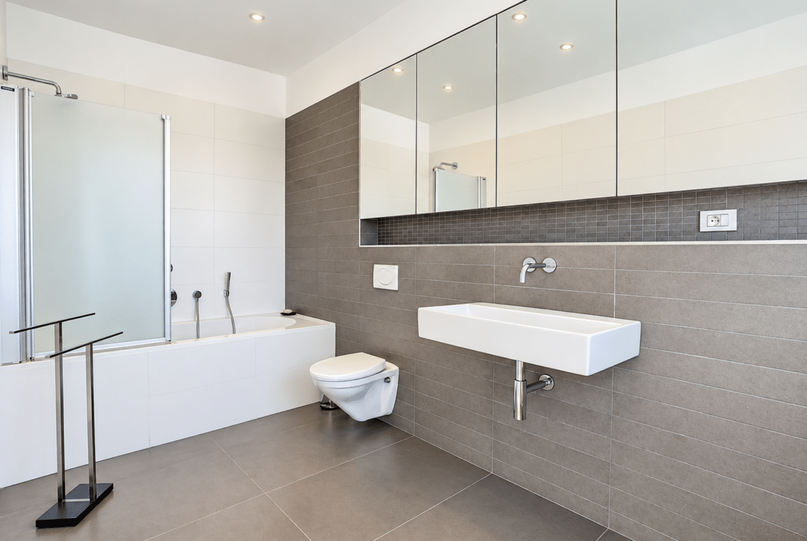 Modern bathroom with a bathtub, glass-enclosed shower, and wall-mounted sink in an apartment.