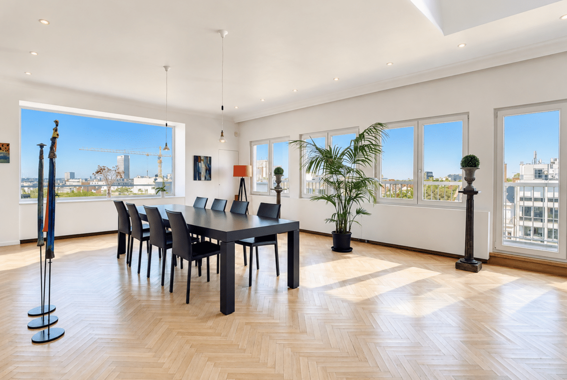 A bright dining room in a modern apartment with hardwood floors, large windows, and a city view.