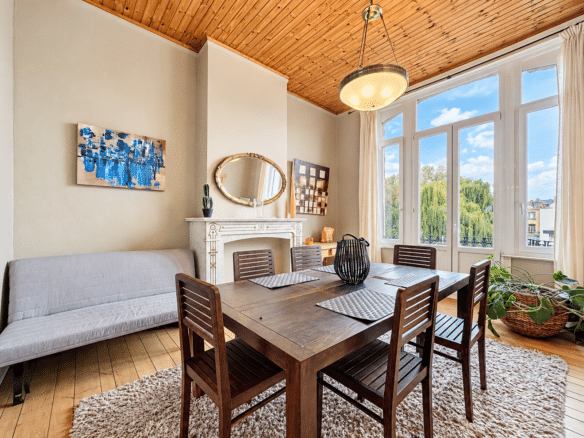 Lichte eetkamer in een appartement met parketvloer, decoratieve open haard en grote ramen   appartement met 1 slaapkamer  Elsene