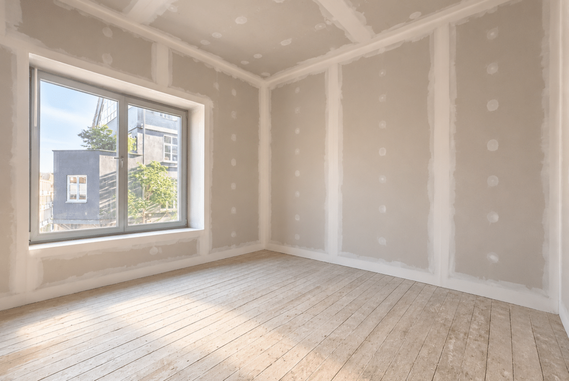 Lichte kamer in een appartement in renovatie, met houten parket en een groot raam.