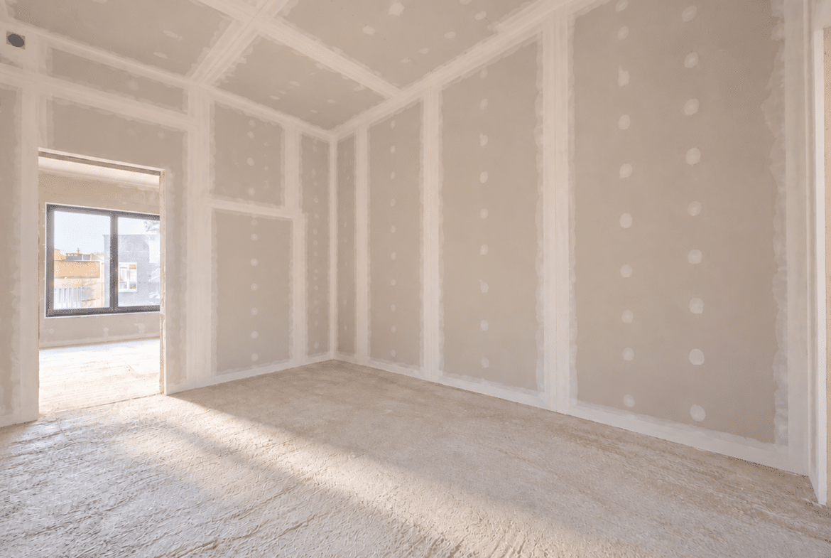 Woonkamer in aanbouw met gipsplaatwanden en natuurlijk licht.
