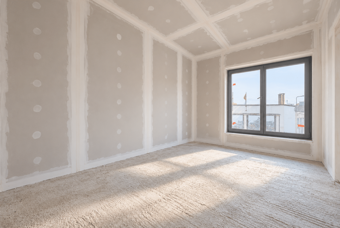 Kamer in een appartement in afbouw, met een groot raam en gipsplaatwanden.