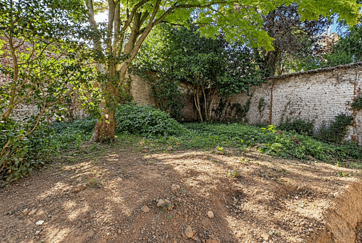 Een omheinde tuin met bomen bij een huis met bakstenen muren.