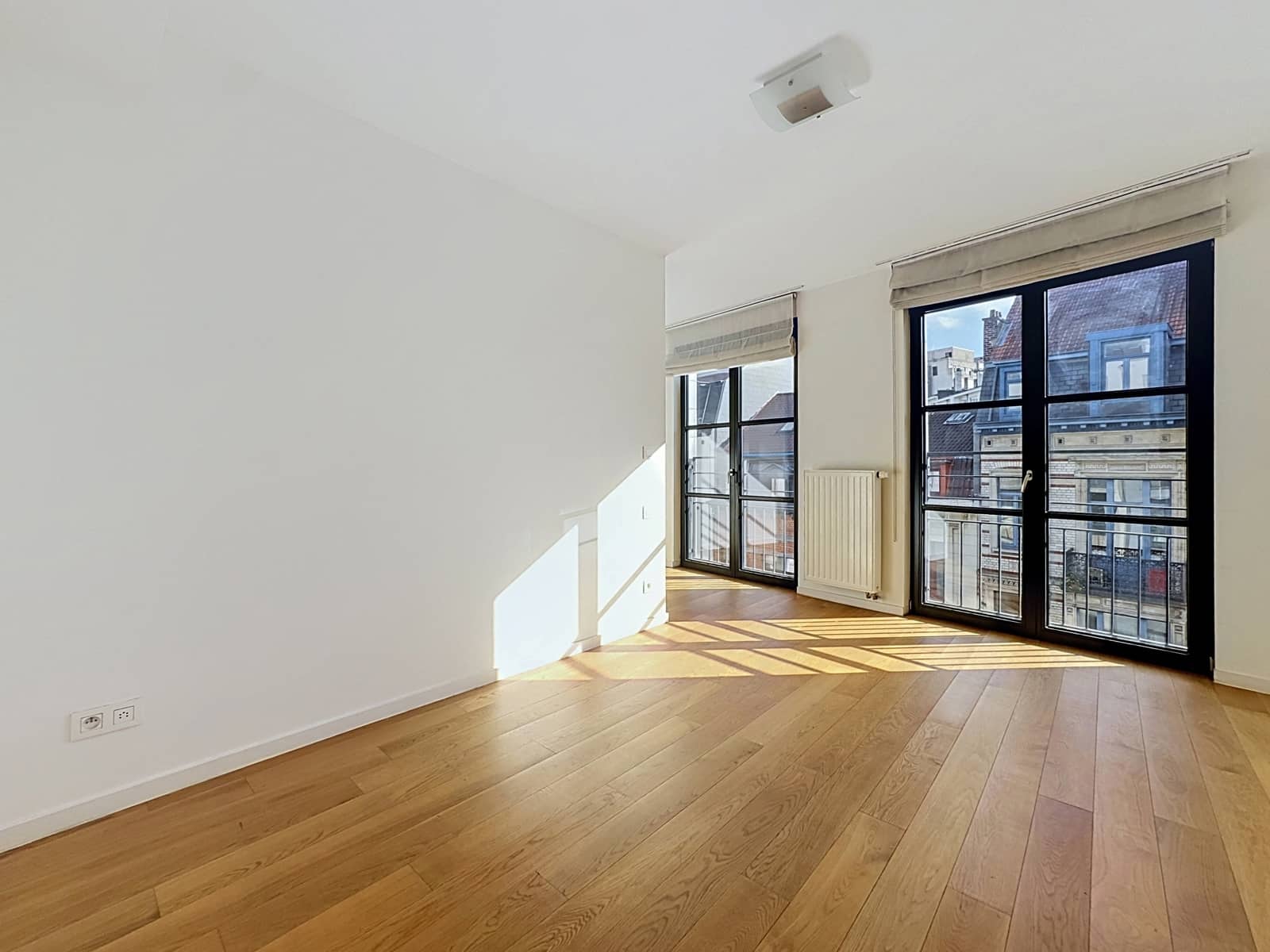 Lichte woonkamer met uitzicht op de stad – You Real Estate Agency Lichte woonkamer met parketvloer, grote ramen en uitzicht op de stad.