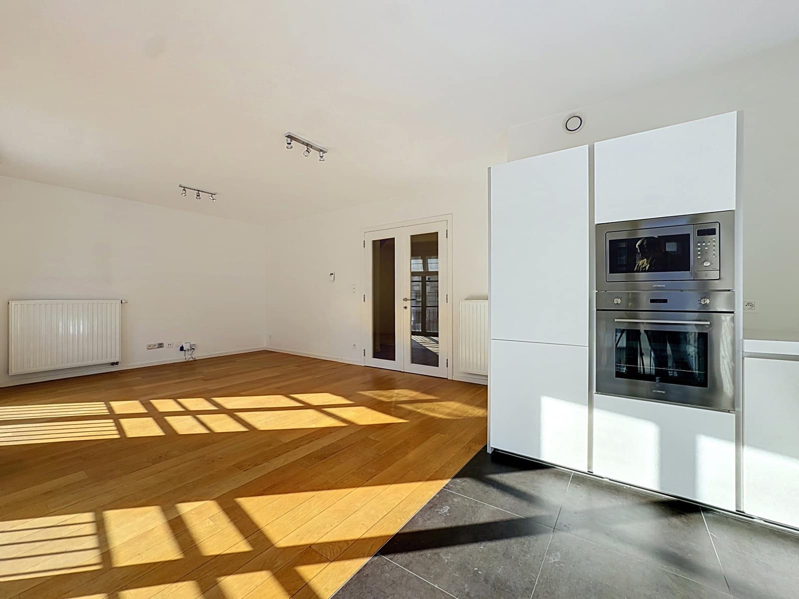 Lichte woonkamer met moderne keuken – You Real Estate Agency Licht appartement met open woonkamer, moderne inbouwkeuken en parketvloer.