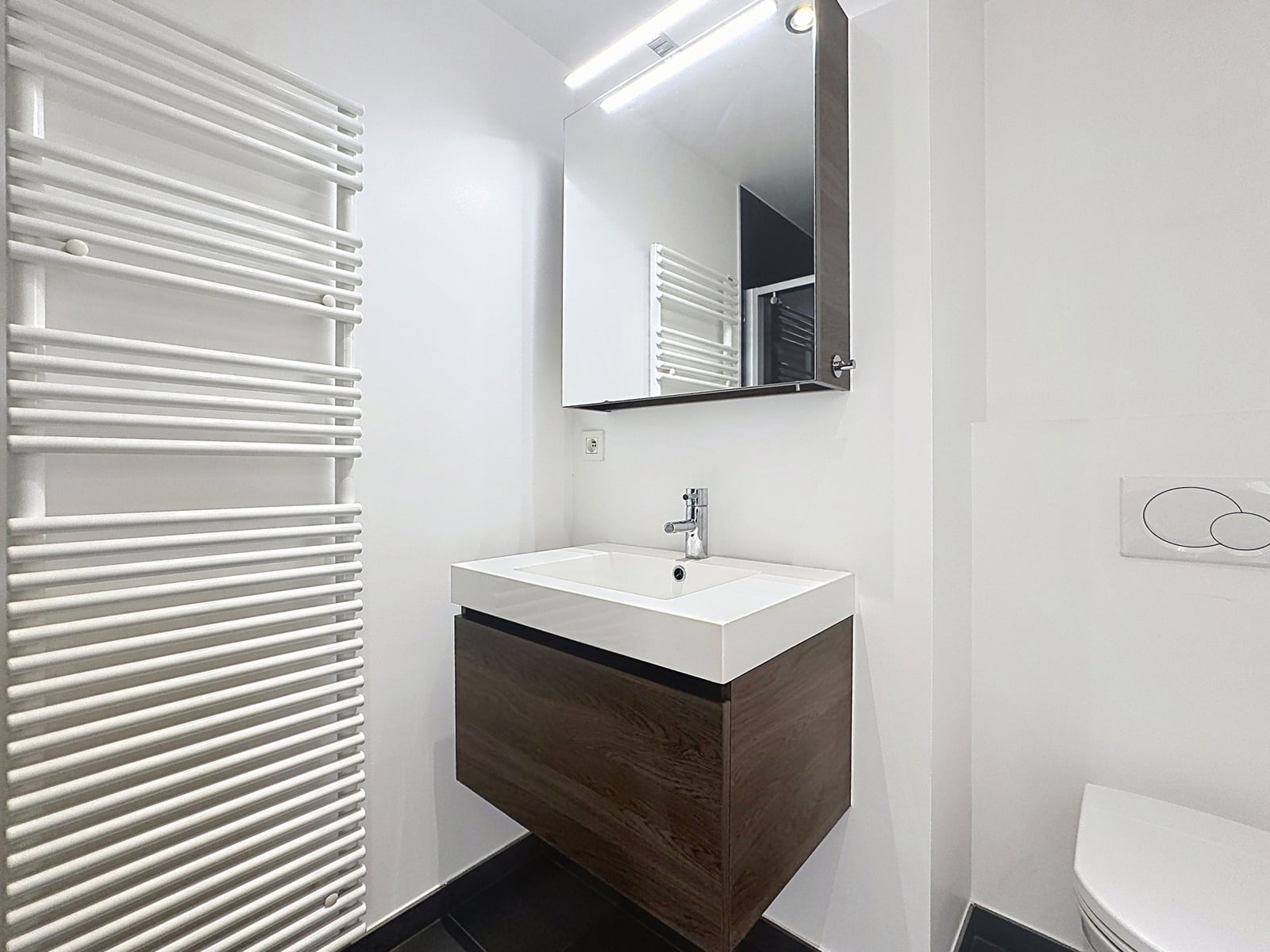 Moderne badkamer - Uw makelaarskantoor Moderne badkamer in een appartement met een hangende wastafelkast en een handdoekradiator.
