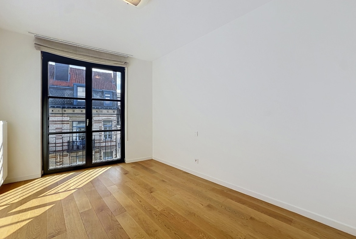Lichte kamer in een appartement met parketvloer, een groot raam en een klein balkon.
