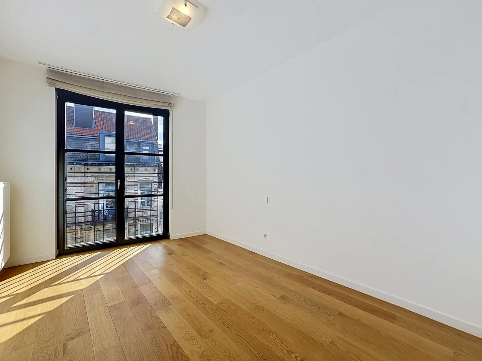 Lichte kamer met parketvloer - You Real Estate Agency Lichte kamer in een appartement met parketvloer, een groot raam en een klein balkon.