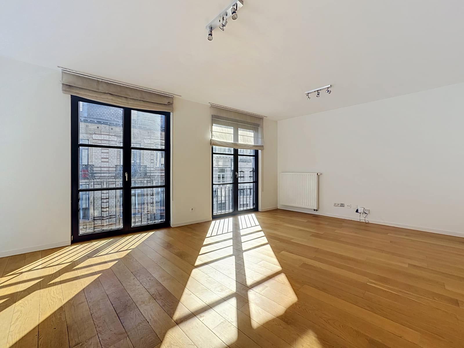 Lichte woonkamer met parketvloer - You Real Estate Agency Lichte woonkamer in een modern appartement met parketvloer, grote ramen en zonwering.