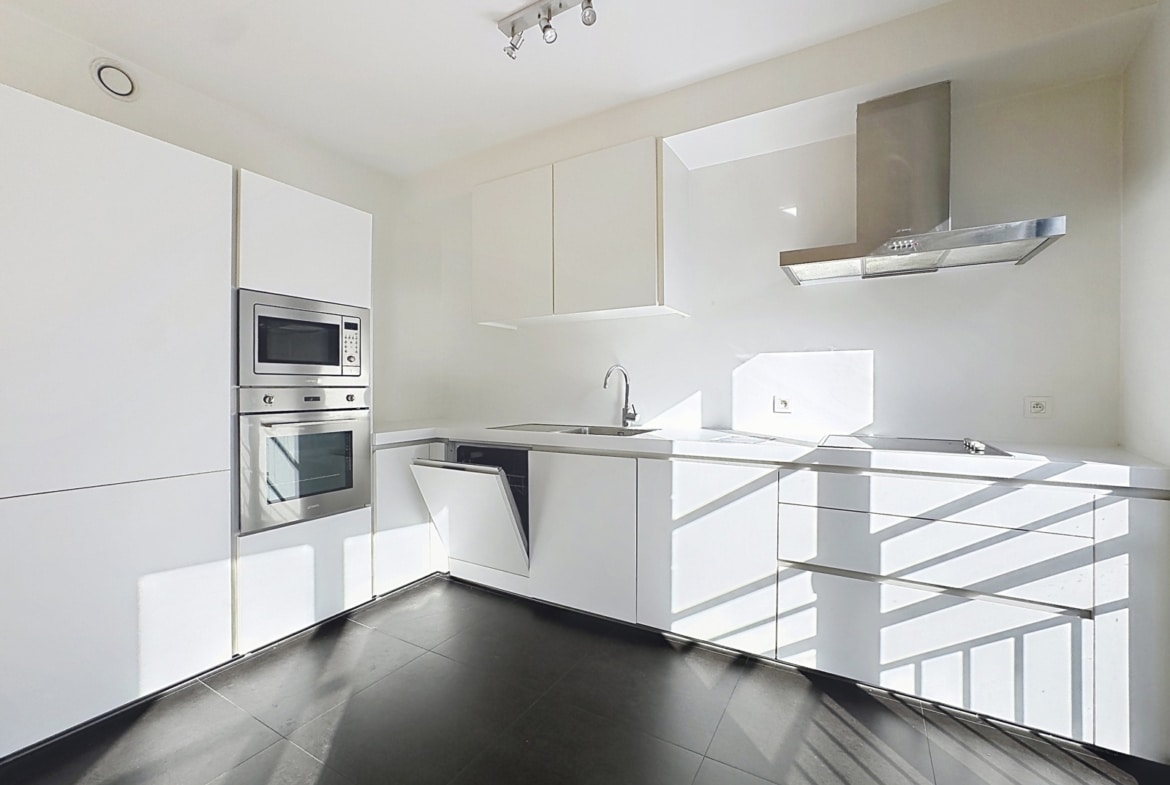 Lichte, moderne keuken met witte opbergruimtes en inbouwapparatuur in een nieuwbouwappartement.